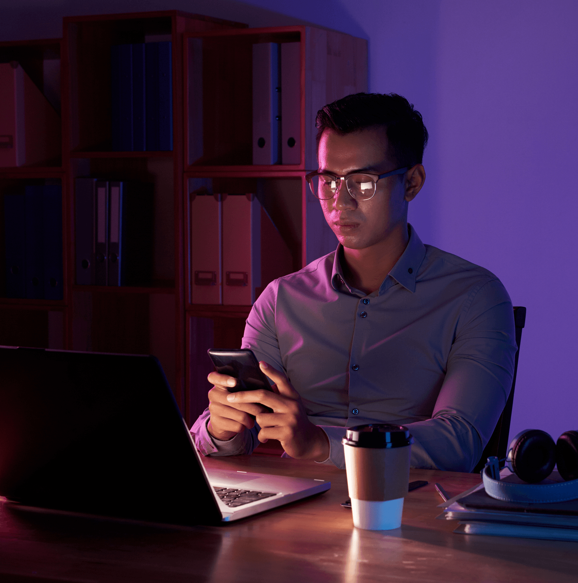man working with laptop and phone under dark purple lighting